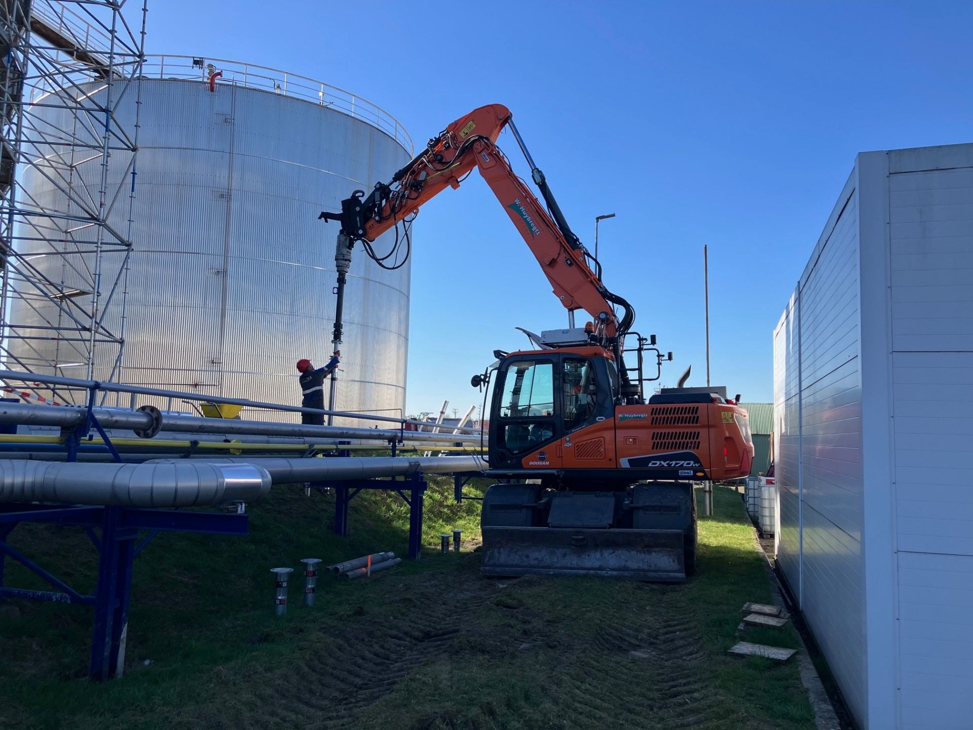 Doosan DX170W met schroefpaal-aandrijving naast opslagtank